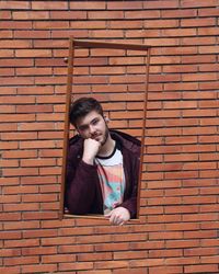 Portrait of young man standing against brick wall