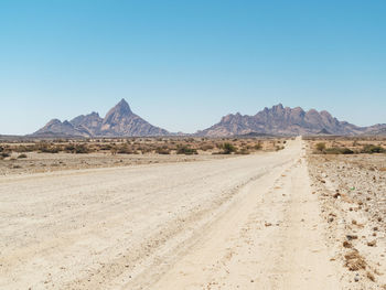 Dirt road in desert against clear sky