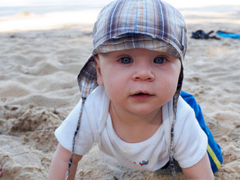 Close-up portrait of baby boy kneeling on sand at beach
