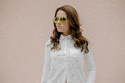 Young woman wearing sunglasses while standing against wall