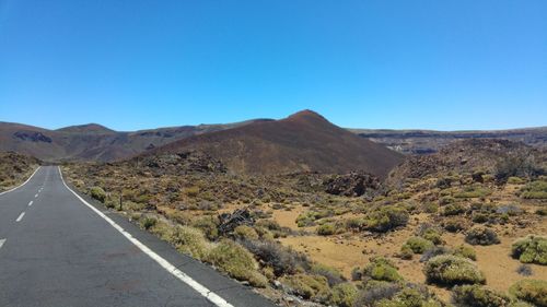 Road leading towards mountains against clear blue sky