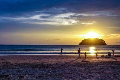 Silhouette people on beach against sky during sunset