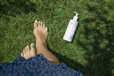 Low section of woman holding bottle on grass