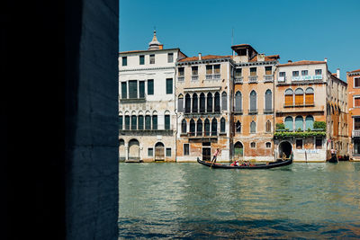 Gondola sailing in grand canal by old buildings against clear blue sky