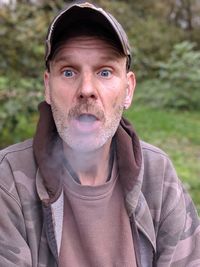 Portrait of man emitting smoke against trees