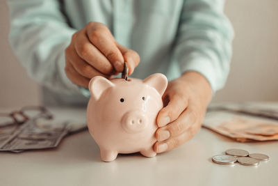 Midsection of man putting coin in piggy bank on table