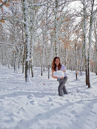 Cheerful woman holding snow in forest during winter