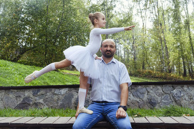 A little ballerina supported by her dad shows an element of ballet on a walk in the park