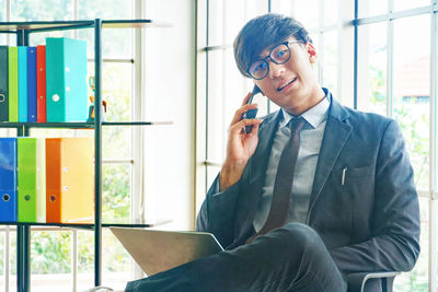 Young man using phone while sitting on window