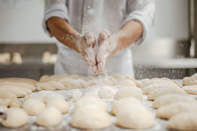 Midsection of chef sprinkling powdered sugar on dough in kitchen