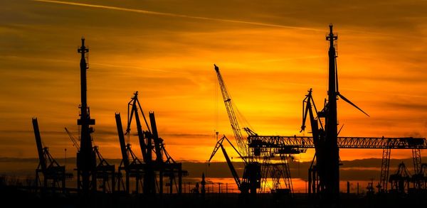 Silhouette cranes against clear sky during sunset