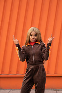 Cheerful african american woman in sportswear dancing in the street on an orange background