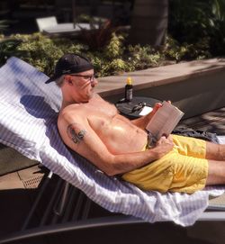 High angle view of mature man sitting on lounge chair and reading book