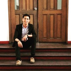 Portrait of young man sitting on steps against door