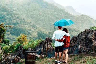 Rear view of man with umbrella against trees