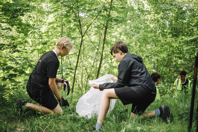 Full length of boy kneeling while collecting plastic together