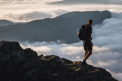 Male hiker on summit gazes at mountain rising above clouds, maine