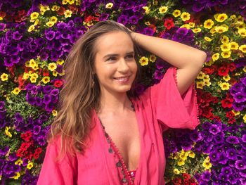 Smiling young beautiful woman standing against petunia flowers