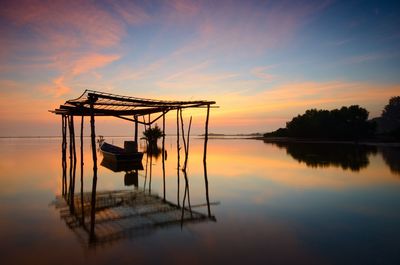 Silhouette cranes by lake against sky during sunset