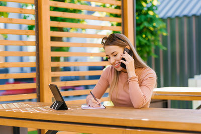 Happy woman freelancer or blogger, entrepreneur is sitting at a table in an outdoor cafe and talking