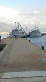 Boats in harbor against cloudy sky