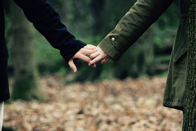 Close-up of couple holding hands at forest during winter