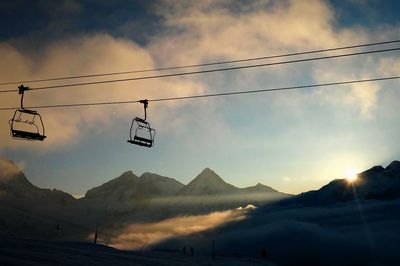 Low angle view of silhouette cable cars over snow covered mountains against sky during sunset