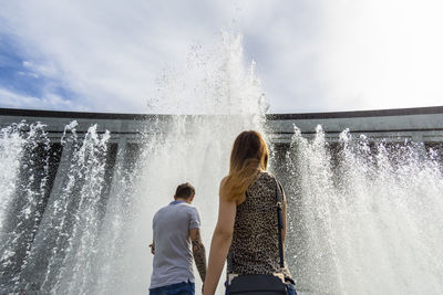 Low angle view of friends standing by splashing water fountain