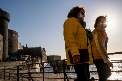 Friends standing by water against clear sky