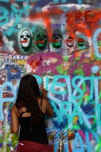 Rear view of woman standing against graffiti wall