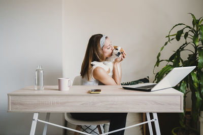 Young woman using phone while sitting on table at home