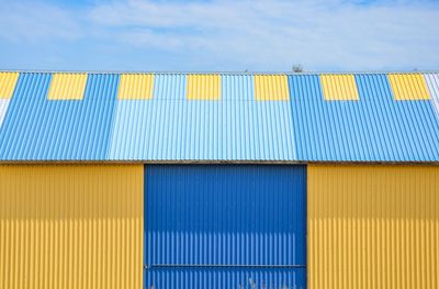 Low angle view of yellow and blue metal building against sky