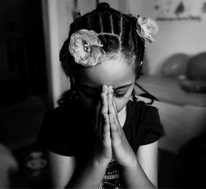 Girl with artificial flower headband praying at home