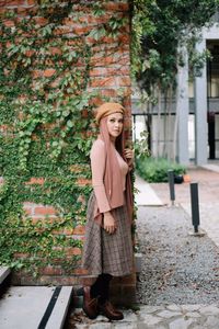 Smiling woman looking away while standing against plants on wall