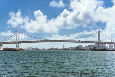 Double-layered suspension rainbow bridge in tokyo bay with the gantry cranes of the port of tokyo.