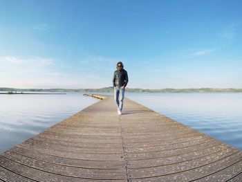 Fish-eye view of man walking on jetty over lake against blue sky
