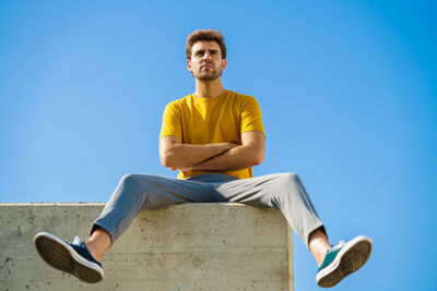 Low angle view of young man sitting against blue sky