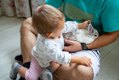 Infant baby girl playing with decorative rabbit in father s hands