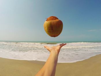 Hand throwing coconut on beach against blue sky