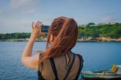 Rear view of woman photographing sea against sky