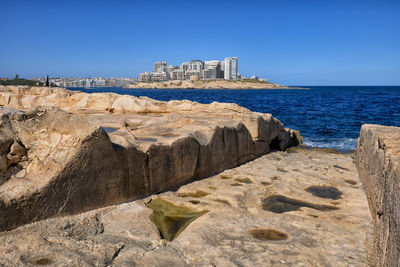 Rocks by sea against clear blue sky