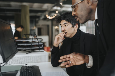 Thoughtful businessman with male colleague discussing over desktop pc at office