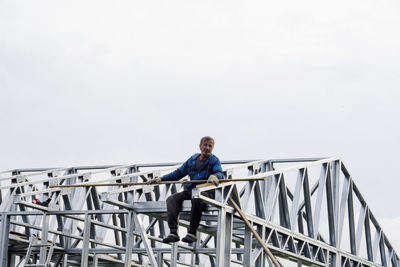 Low angle view of man sitting on bridge against sky