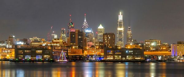 Illuminated buildings by river against sky at night