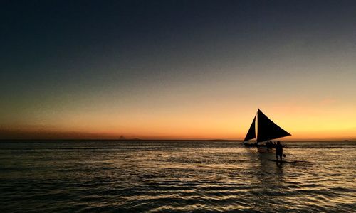 Silhouette sailboat in sea against clear sky during sunset