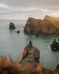 Womn sitting on rock by sea against sky