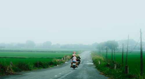 Rear view of people riding motorcycle on road against clear sky