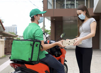 Delivery person wearing mask giving parcel to woman outside home