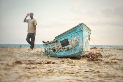 Man saluting while standing by boat at beach against sky