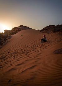 Man sitting on desert against sky